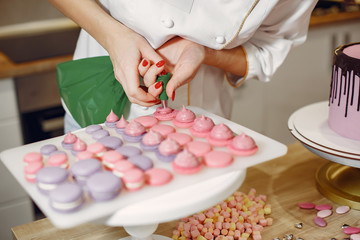 Obraz na płótnie Canvas Confectioner in a kitchen. Woman in a uniform. Professional decorates the macaroni.