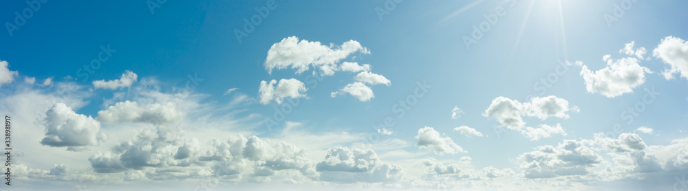 Wall mural sunny blue sky with fluffy clouds. sunlight with rays illuminates the sky. beautiful ultra-wide pano