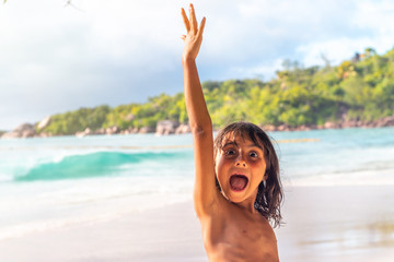 Young girl raising arm happy, standing along a beautiful tropical beach. Vacation and holiday concept