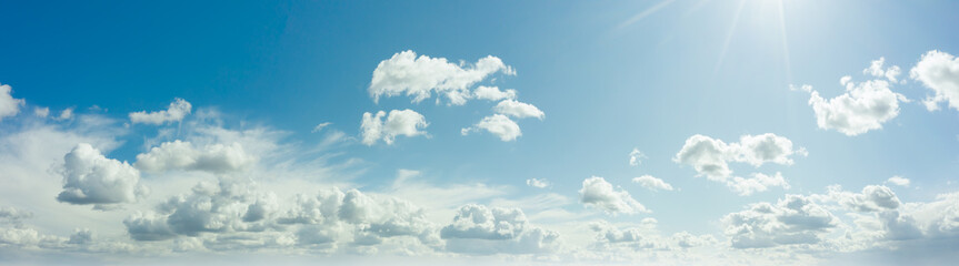 Sunny blue sky with fluffy clouds. Sunlight with rays illuminates the sky. Beautiful ultra-wide...