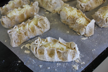 Stage of preparation of Karelian pies -Pirakka. Pies are located on a wooden board, being filled ready for baking. Dish of national cuisine - piirakka. Close-up.