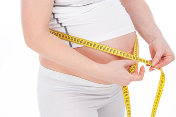 Closeup Pregnant Caucasian Woman Belly. Posing With Yellow Measurement Tape In White Shirt And Pants Against Pure White Background.