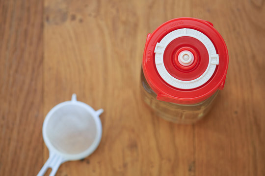 An Overhead Shot Of A Glass Jar Containing Water Kefir And Sealed With A Bright Red Fermentation Lid Indicating The Current Date.