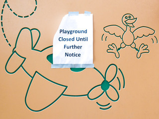 a paper sign at the whimsical entrance wall of an outdoor playground saying that it is closed until further notice