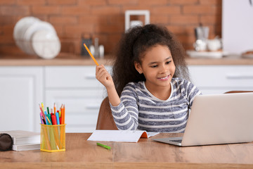 Little African-American girl doing homework in kitchen