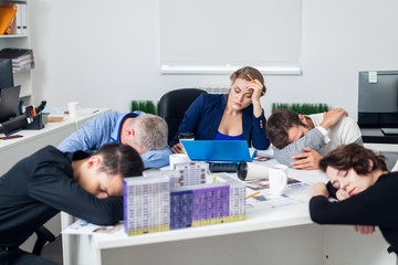 A young business woman trying to concentrate in the office, while her colleagues are having a rest at the meeting table