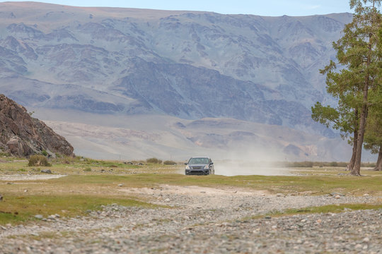 A Large Cloud Of Road Dust Behind A Car Racing Across The Steppe. Mountains In The Background