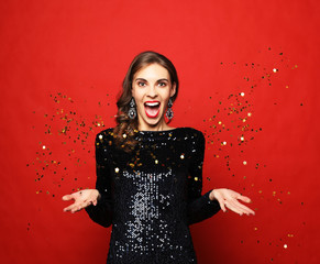 Holiday concept: beautiful brunette female wearing evening dress standing under confetti rain over...