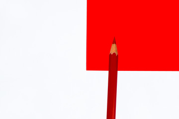 Single wood pencil crayon of red color placed on top of a red white background