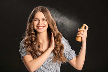 Beautiful young woman with hair spray on dark background