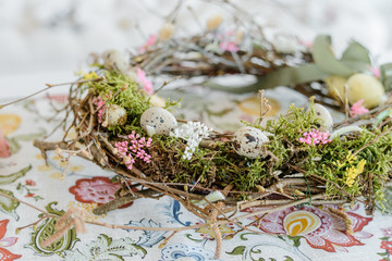 Festive table with a floral tablecloth, wreath of branches, colorful easter eggs. Home decoration. Selective focus. ?lose up