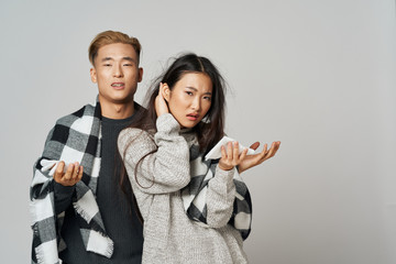 A cheerful young couple of Asian appearance hiding behind a blanket of coolness, a cold of discontent