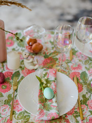 Obraz na płótnie Canvas Decorative festive table setting with floral tablecloth, egg, dish and golden cutlery, glass for wine, willow branch. Happy easter holidsy concept.