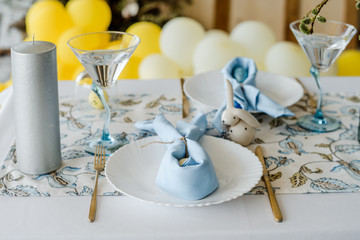 Festive table setting for traditional dinner. sky blue textile napkin, floral tablecloth, easter eggs, golden fork and knife, willow. Yellow balloons party decoration
