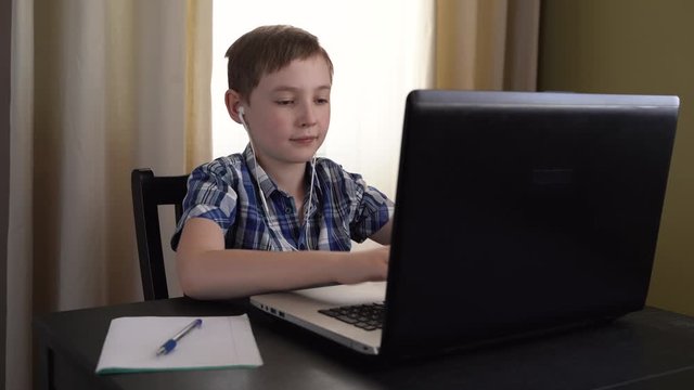 4k. a Schoolboy in a checked shirt is successfully doing homework using a laptop, sitting at home and carefully reading information on the computer screen. Internet technology .