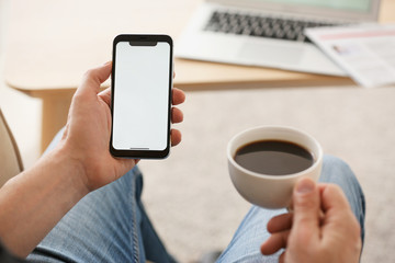 Young man with mobile phone drinking coffee at home