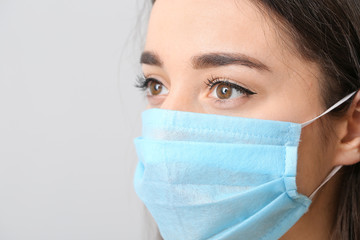 Young woman wearing medical mask against grey background