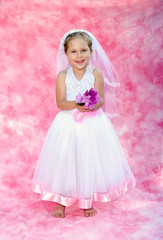 Little girl dressed as a  bride  poses on  a soft pink backdrop