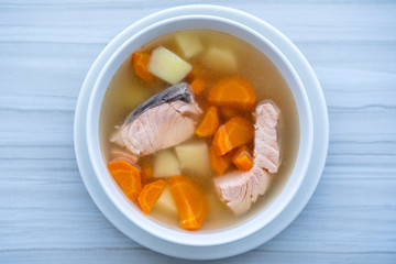 Fresh salmon fish soup with carrots, potatoes and onions in a white plate, close up. Tasty dinner consists of a fish soup with salmon