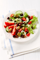 Healthy salad with various tomatoes, cucumber, olives and capers. White wooden background. 