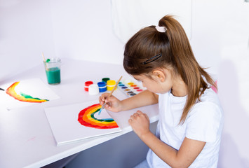 Stay at home due coronavirus pandemic concept. Little girl paints a rainbow on stay at home poster. Chase the rainbow flashmob. Stay home during a pandemic.. COVID - 2019