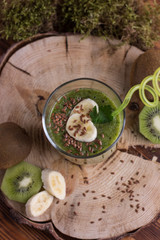 Homemade green smoothie with parsley banana and kiwi with flax seeds in a glass with a straw on a wooden saw