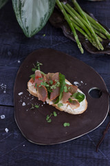 Bruschetta with cream cheese and ham on a plate and asparagus in the background