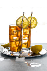 Two backlit glasses of ice tea with lemon slices ready for drinking.