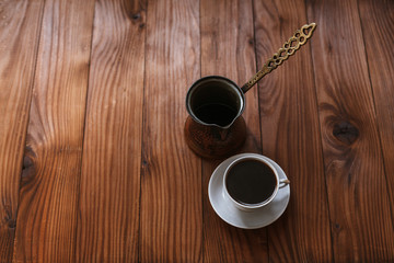 Traditional copper turkish coffee pot and hot aromatic coffee in a white porcelain cup on a saucer on a wooden table in the morning, top view.