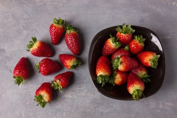 Red fresh big strawberries on a dark plate and on a grey table
