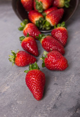 Red fresh big strawberries on a dark plate and on a grey table