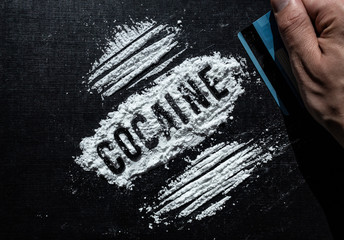 Closeup to a male hand hand holding a credit card making cocaine lines over a black background....