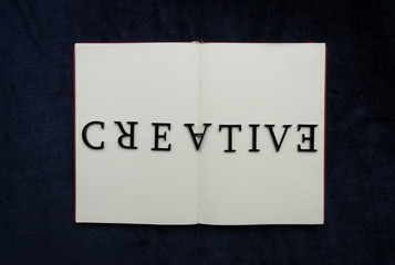 Close up to CREATIVE lettering over blank notebook at blue navy background.  Reading and study concept photography