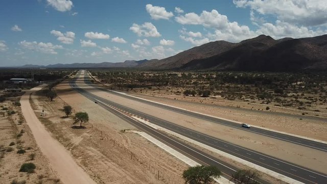 4K aerial video of newly upgraded main A1/B1 highway outside Windhoek to town Okahandja with bush covered mountains, dry endless savanna view, metal silo towers in Khomas Region, central Namibia