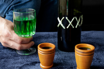 Close up to a man holding a cup of green homemade liquor with two wooden cups and green artesanal alcohol bottle. Party and liquor concept
