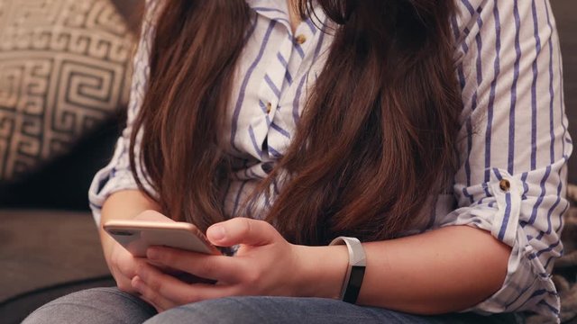 Caucasian young woman using her mobile phone phone devise on her living room couch at home