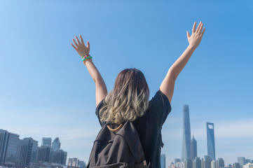 Fototapeta na wymiar Asian girl traveller with dyed hair raises her hands and waving hands looking far away with the background of the Shanghai Lujiazui Cityscape and sky scrappers skyline in the sunny day
