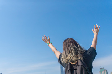 Asian girl traveller with dyed hair raises her hands and waving hands looking far away with the background of the Shanghai Lujiazui Cityscape and sky scrappers skyline in the sunny day