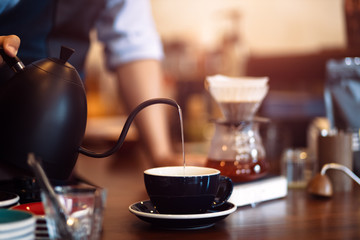 barista pouring boiling water from kettle to drip coffee maker.