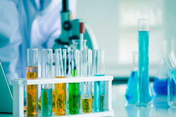 Close-up shot of science laboratory test tubes. Liquid many colors in equipment glassware for chemistry biology samples. Blur background is scientist experimenting with tube and microscope.