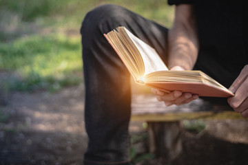 Man sitting on a bench and reading a book outside in the park. Male hands holding a book outdoor....