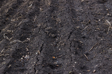 Black soil after snow, before sowing. Earth texture, rustic background. Close-up of a spring field plowed with furrows.