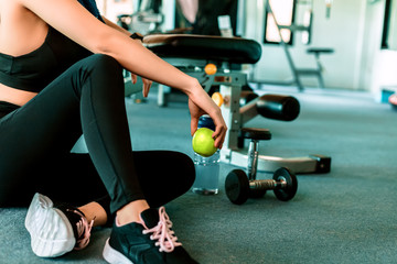 Fototapeta na wymiar Woman exercise in gym fitness breaking and relax. hand holding apple fruit after training sport and dumbbell, water bottle on the ground.