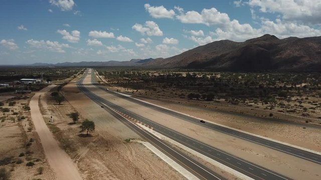 4K aerial video of newly upgraded main A1/B1 highway outside Windhoek to town Okahandja with bush covered mountains, dry endless savanna view, metal silo towers in Khomas Region, central Namibia