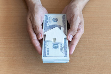 Man hands holding 100 dollar bills and house on wooden table. Concept of saving money.