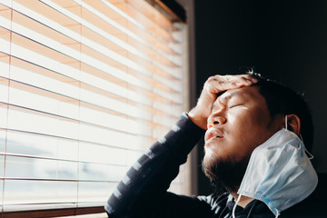 Asian man in isolation have a headache. Man in medical mask forced to stay inside the house as a...