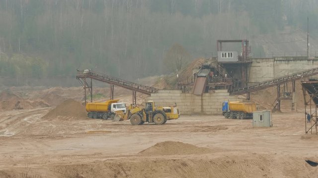 Trucks machine works in the sand ballast quarry on the cloudy summer day