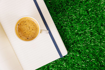 Blank open notepadand coffee cup espresso on a green grass