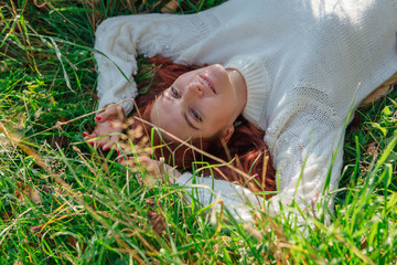 Beautiful happy woman laying in grass in white sweater