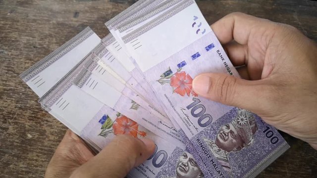 Hand calculates the banknote Ringgit Malaysia, value of the 100 on the wooden table. (selected focus)